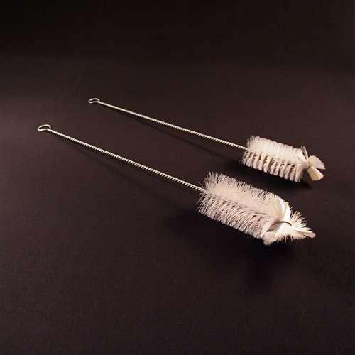 Two long metal cleaning brushes with white bristles and looped handles, photographed on a dark brown background.