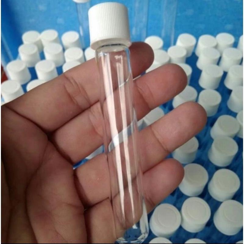 A hand holding a clear glass vial with a white screw cap, with many similar vials in a blue tray in the background.